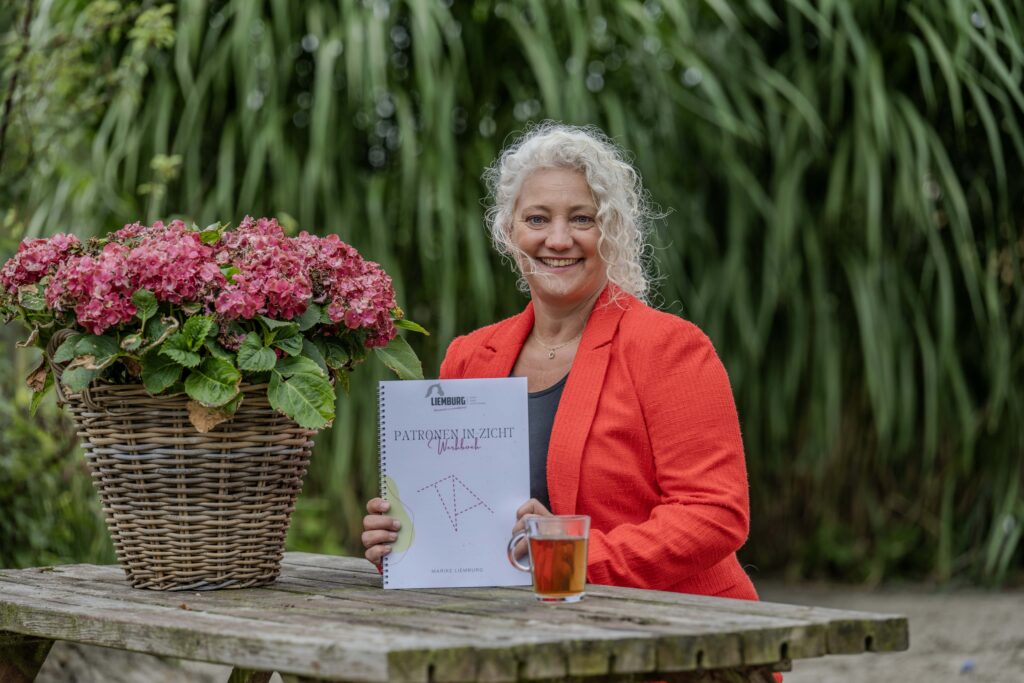 Marike met werkboek patronen in zicht aan een tuintafel
